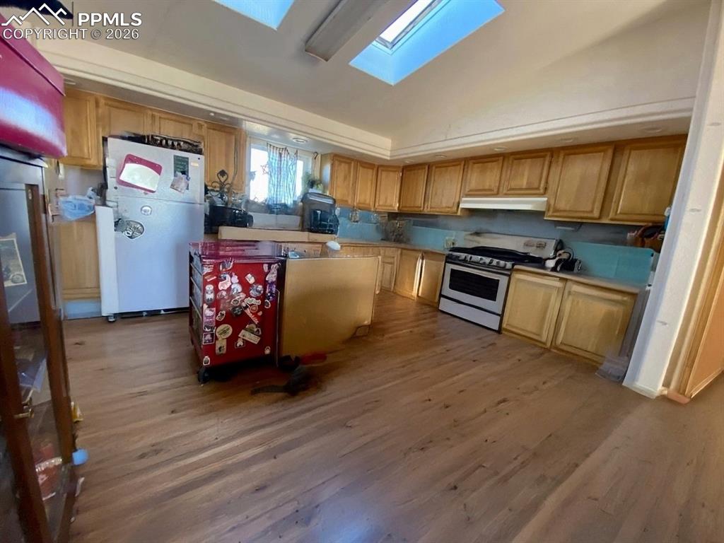 Kitchen featuring a skylight, freestanding refrigerator, gas stove, dark wood-style floors, and light countertops
