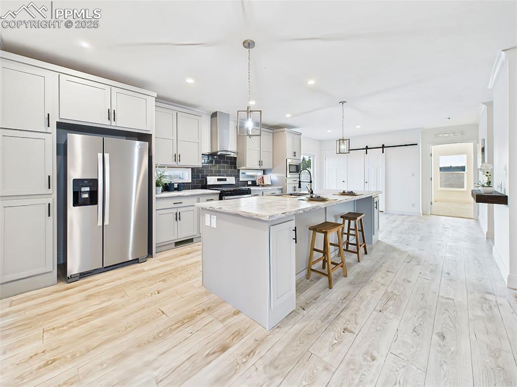 Modern kitchen with stainless steel appliances, shaker cabinetry, sliding barn door pantry, and durable luxury vinyl flooring extending to the entryway.