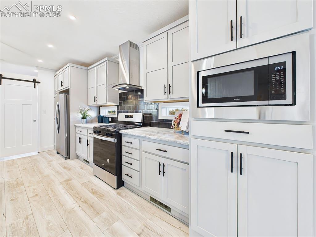 Stylish combination of light gray cabinetry, tile backsplash, and barn door pantry for added character and functionality. Stainless steel gas range with vent hood and coordinating tile backsplash for a clean, upscale look.