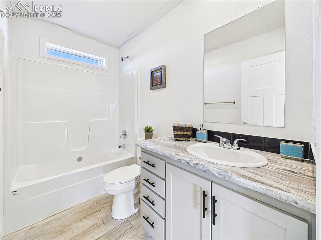 Bright full bath with single-sink vanity, wood-look tile floors, and modern fixtures.