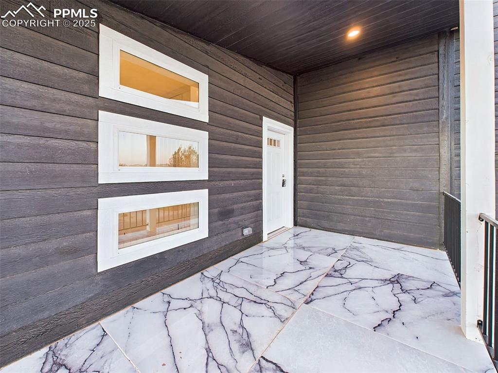 Distinctive front entry with modern dark siding, recessed lighting, and sleek marble-look tile flooring.