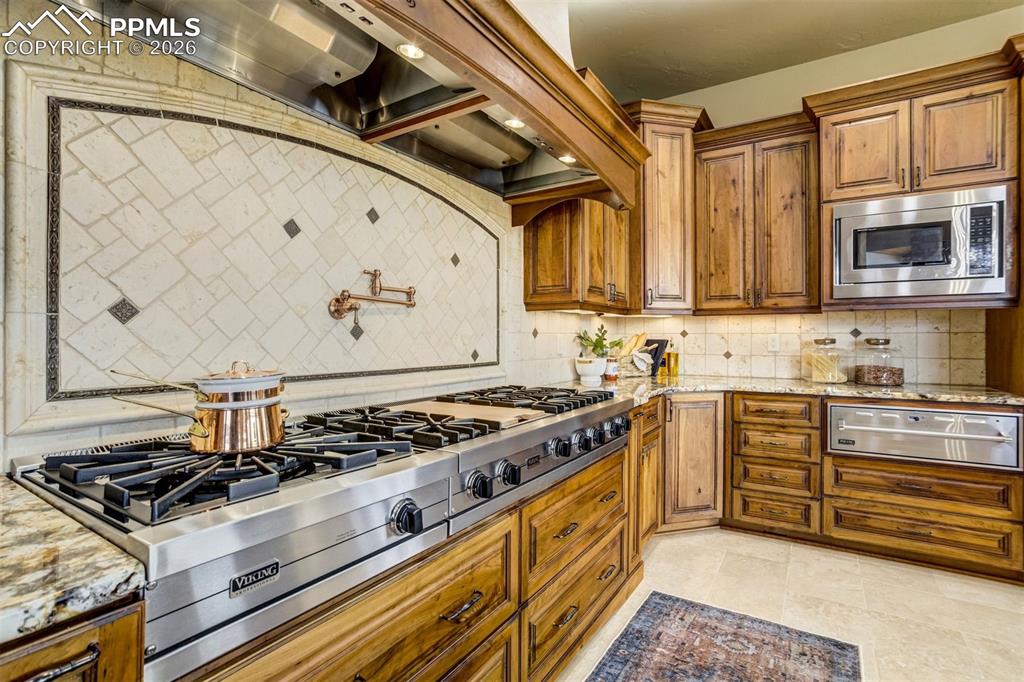The oversized gas cooktop, complete with a convenient pot filler and custom tumbled stone backsplash, brings both beauty and function to this thoughtfully designed kitchen workspace