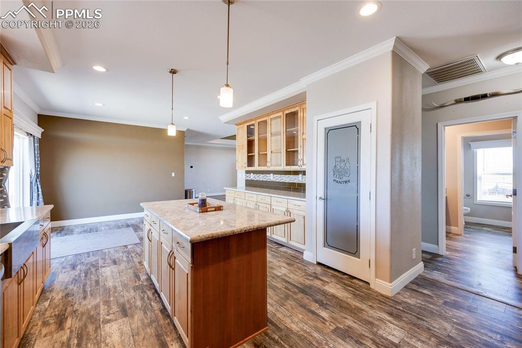 Kitchen featuring healthy amount of natural light, ornamental molding, decorative light fixtures, glass insert cabinets, and a center island