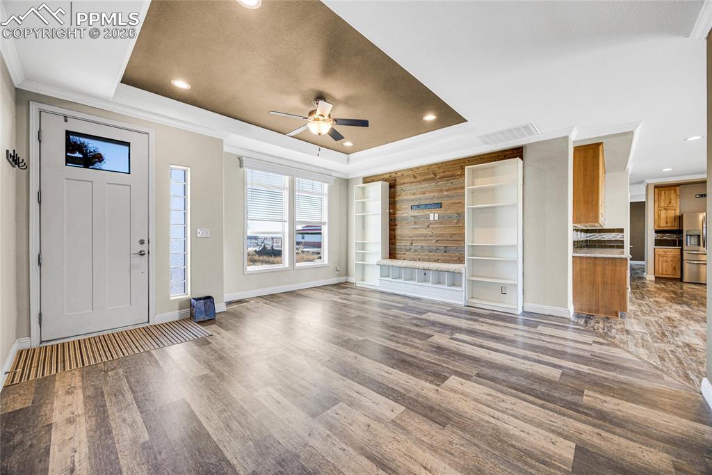 Unfurnished living room with ceiling fan, crown molding, wood finished floors, a raised ceiling, and recessed lighting
