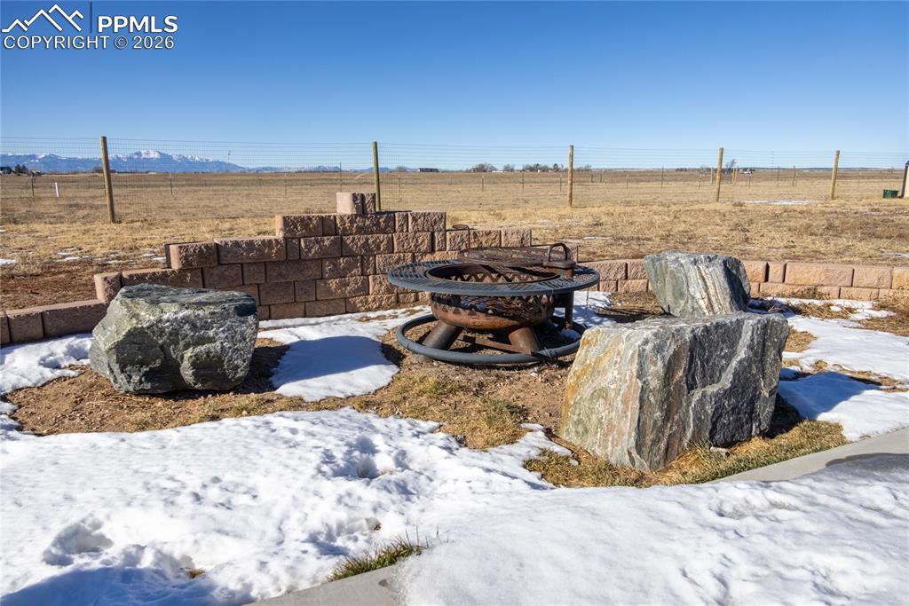 Yard layered in snow featuring an outdoor fire pit and a view of countryside