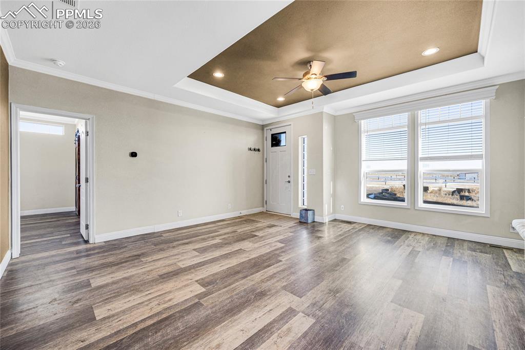 Unfurnished living room featuring crown molding, a tray ceiling, ceiling fan, light wood-style flooring, and recessed lighting