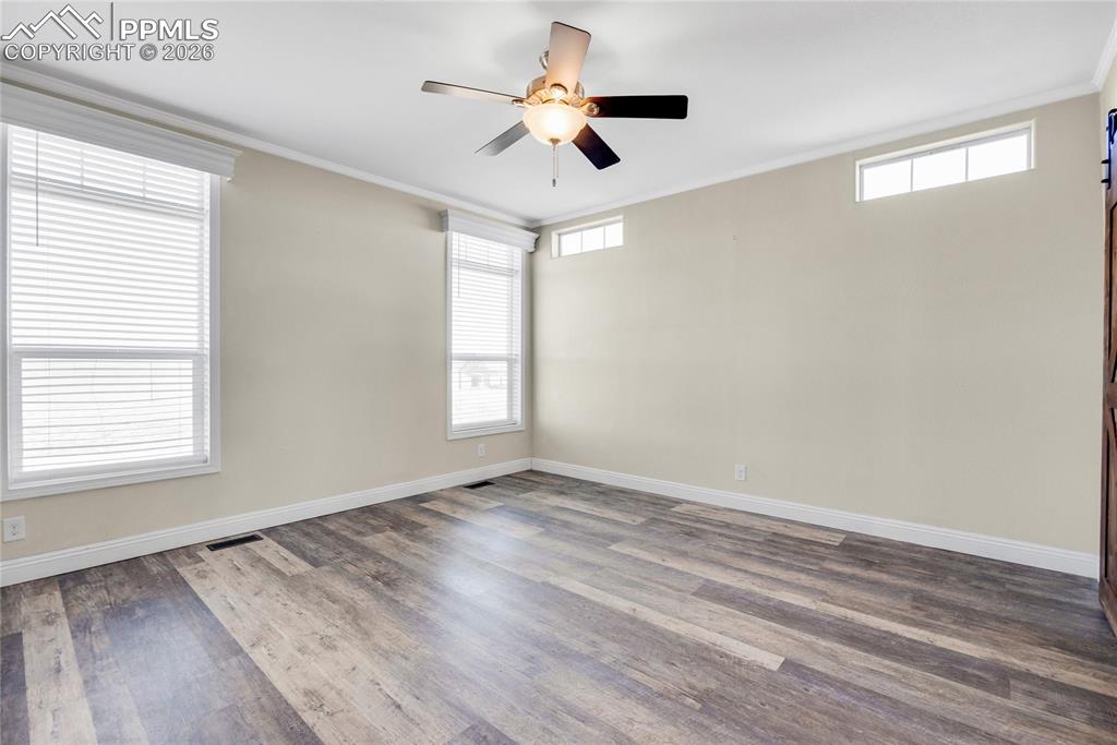 Empty room with ornamental molding, dark wood-type flooring, plenty of natural light, and a ceiling fan