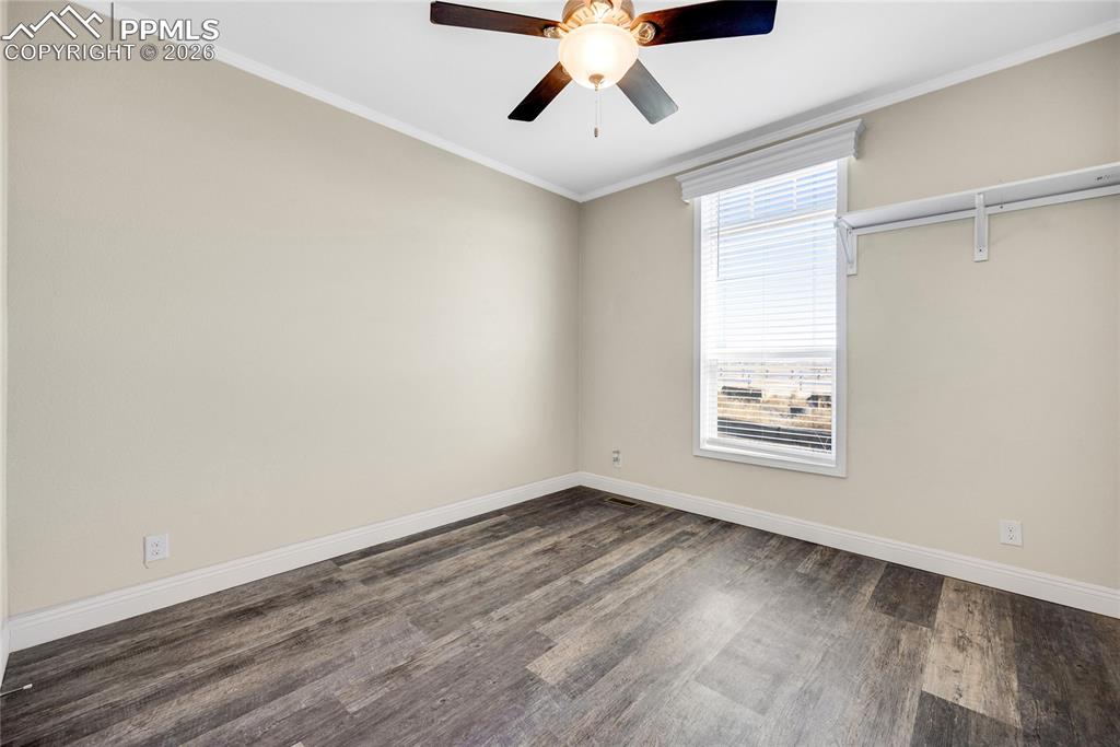 Empty room featuring crown molding, dark wood-style floors, and ceiling fan
