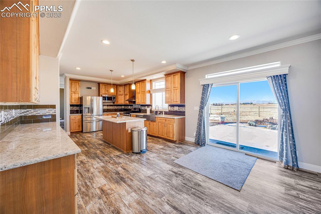 Kitchen featuring a kitchen island, pendant lighting, stainless steel appliances, dark wood-style flooring, and light stone countertops