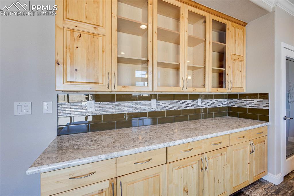 Kitchen with light brown cabinetry, glass insert cabinets, and backsplash