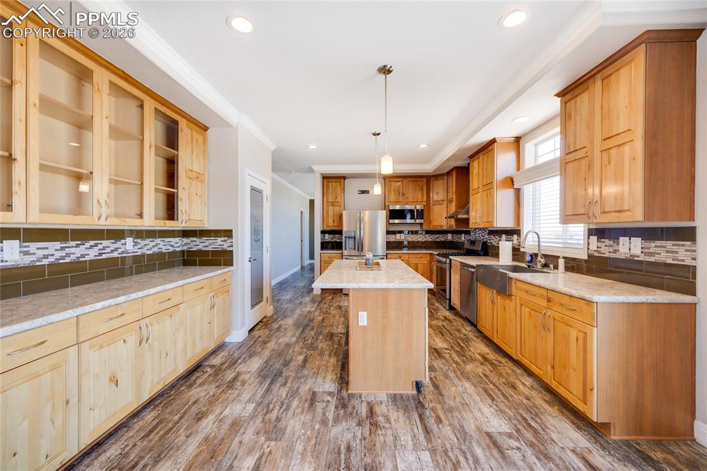 Kitchen featuring decorative backsplash, glass insert cabinets, pendant lighting, dark wood-style flooring, and crown molding