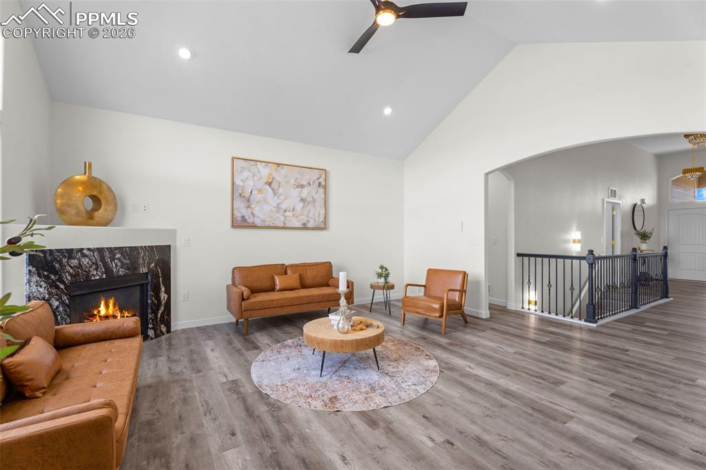 Living area with ceiling fan, a fireplace, vaulted ceiling, arched walkways, and wood finished floors