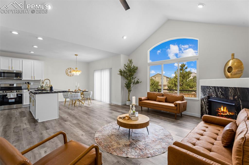 Living area featuring a high ceiling, wood finished floors, a high end fireplace, a ceiling fan, and hanging lights