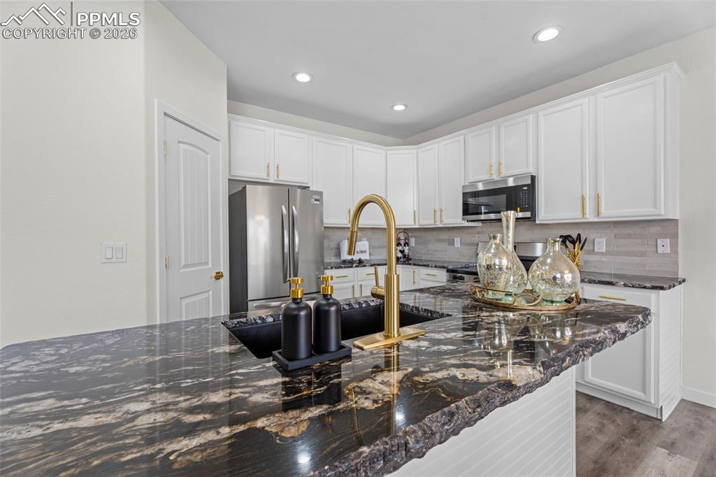 Kitchen with white cabinets, dark stone counters, stainless steel appliances, wood finished floors, and recessed lighting