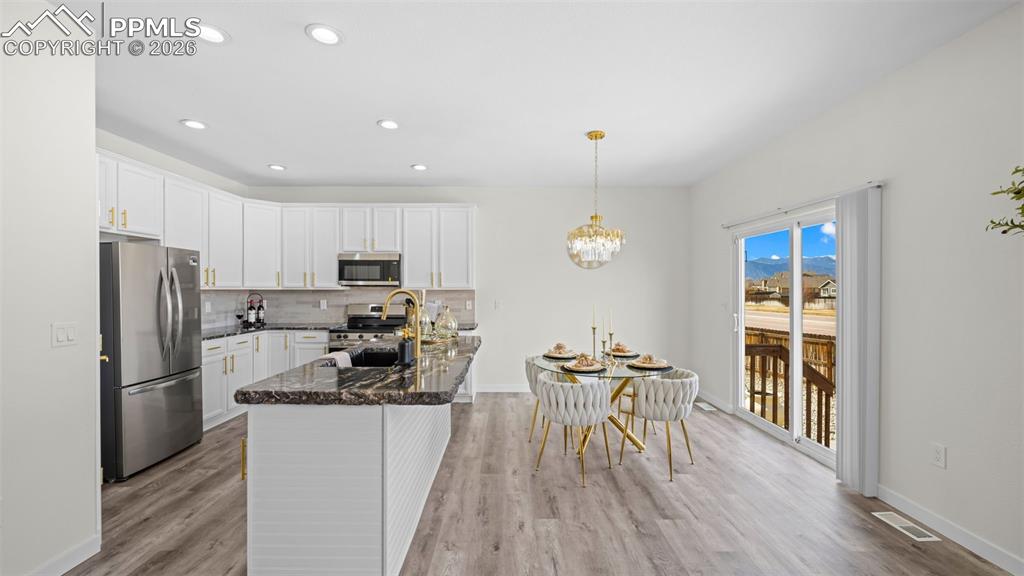 Kitchen with stainless steel appliances, white cabinets, backsplash, dark stone countertops, and light wood-style flooring