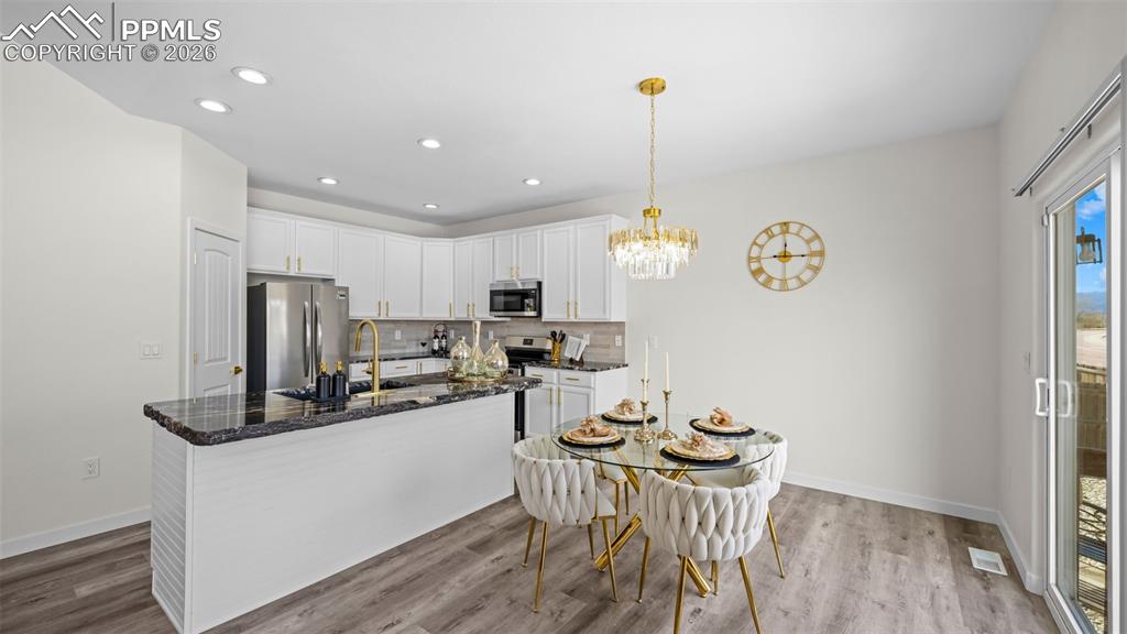Kitchen featuring dark stone counters, white cabinetry, stainless steel appliances, a kitchen island with sink, and dark wood-type flooring