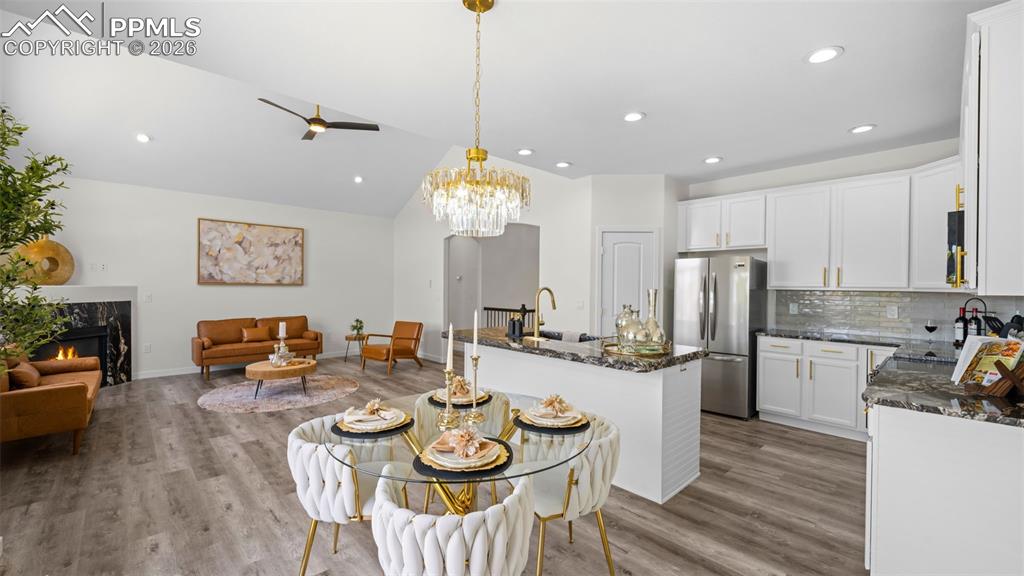 Dining space with a fireplace, light wood finished floors, ceiling fan, vaulted ceiling, and suspended lighting