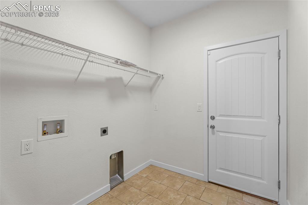 Laundry area with electric dryer hookup, hookup for a washing machine, and light tile patterned flooring