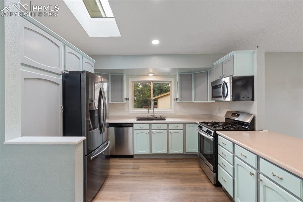 Kitchen with light countertops, a skylight, stainless steel appliances, recessed lighting, and light wood-type flooring