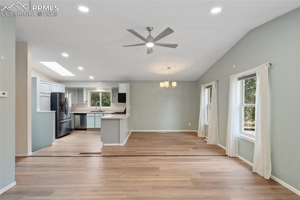 Open concept main level Kitchen, Dining room, and Living room light wood-style floors and vaulted ceiling