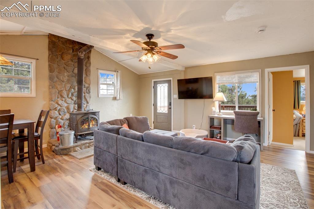 Living area with a wood stove, healthy amount of natural light, light wood-style flooring, and a ceiling fan