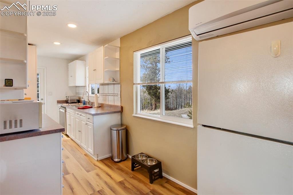 Kitchen featuring open shelves, an AC wall unit, white microwave, white cabinets, and light wood-style floors
