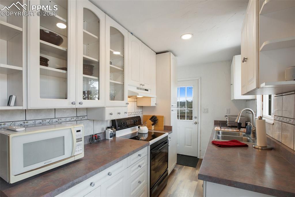 Kitchen with black electric range, white cabinetry, white microwave, dark countertops, and open shelves