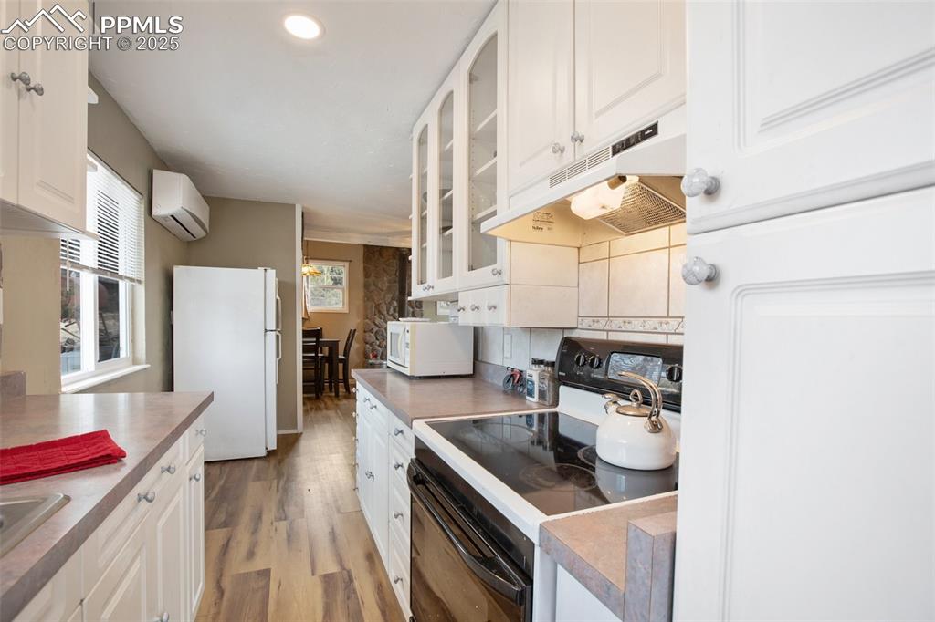 Kitchen featuring white cabinets, white appliances, under cabinet range hood, light wood-style flooring, and glass insert cabinets