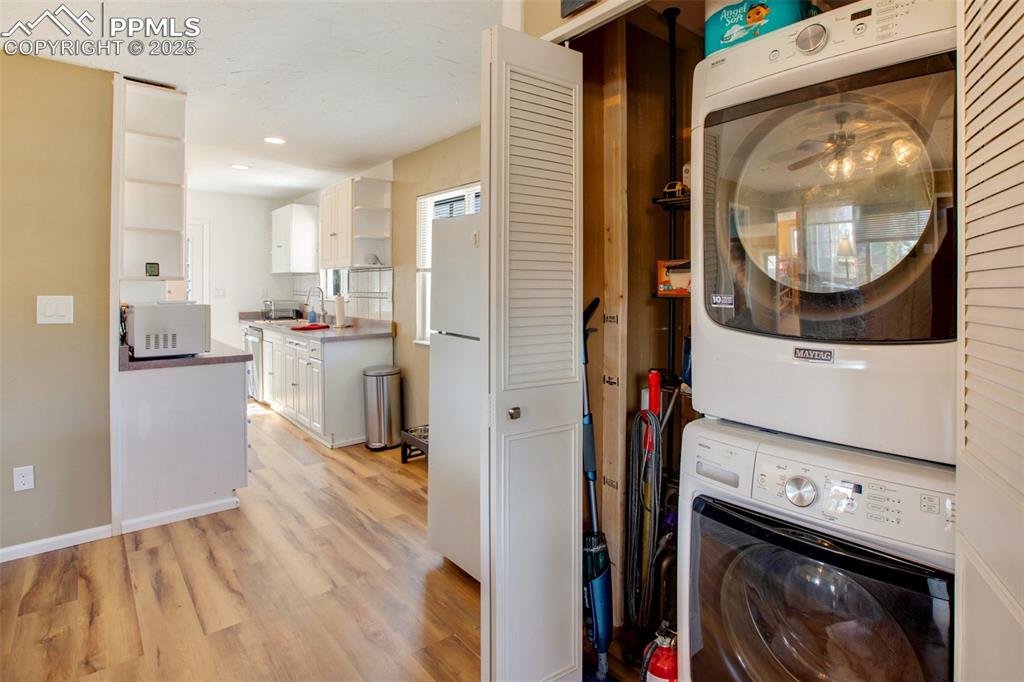 Laundry area featuring stacked washer and clothes dryer, light wood-type flooring, and ceiling fan