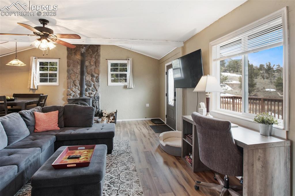 Living room with a wood stove, vaulted ceiling, light wood-type flooring, healthy amount of natural light, and a ceiling fan