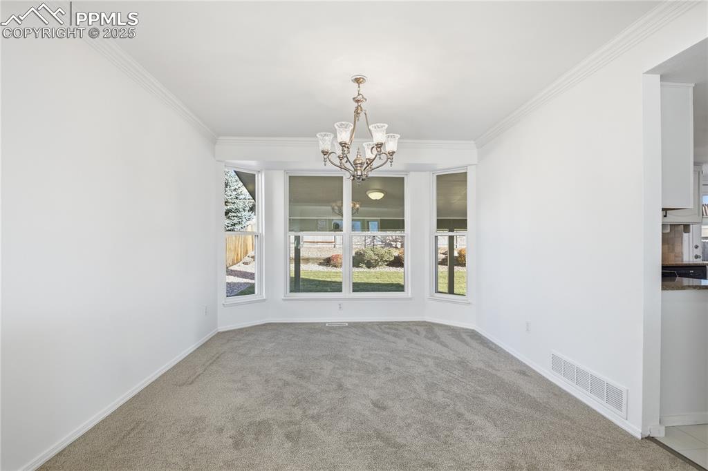 Unfurnished dining area featuring a chandelier, crown molding, and carpet floors