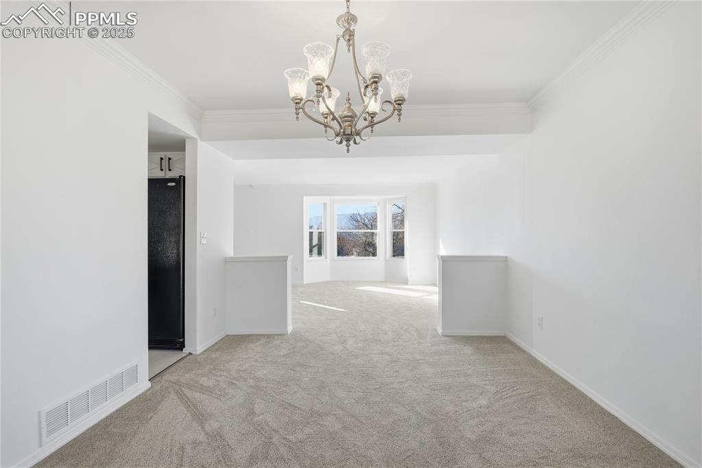 Spare room featuring ornamental molding, light colored carpet, and a chandelier