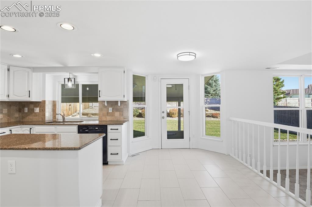 Kitchen with dark stone counters, tasteful backsplash, white cabinets, healthy amount of natural light, and recessed lighting