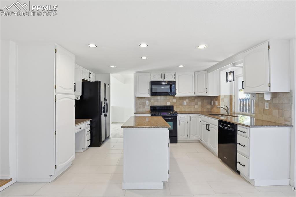 Kitchen featuring dark stone counters, backsplash, black appliances, white cabinetry, and recessed lighting