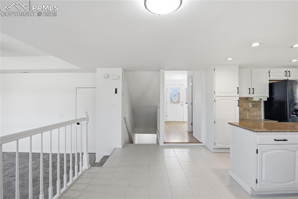 Kitchen with white cabinets, dark stone countertops, black refrigerator with ice dispenser, recessed lighting, and tasteful backsplash