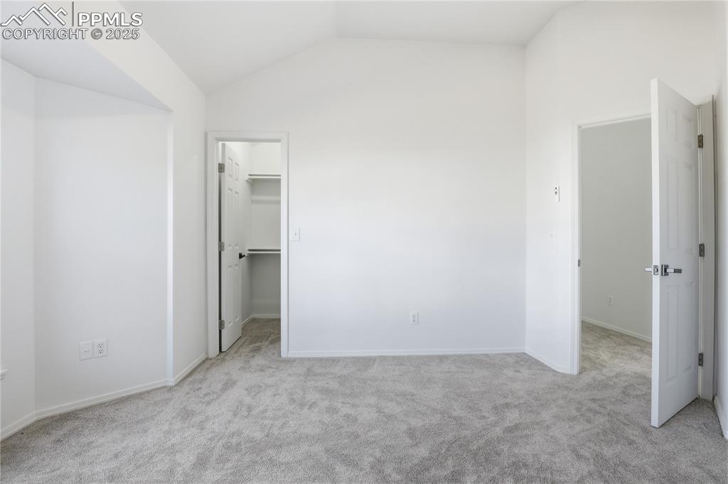 Unfurnished bedroom with vaulted ceiling, a walk in closet, and light colored carpet