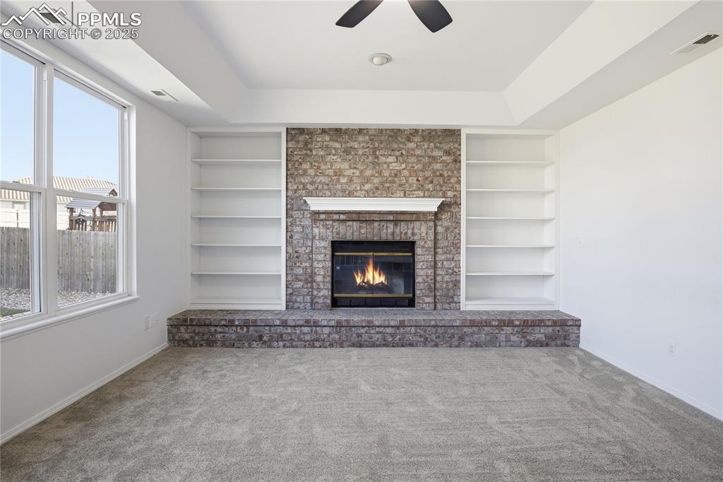 Unfurnished living room with ceiling fan, carpet flooring, a fireplace, and built in shelves