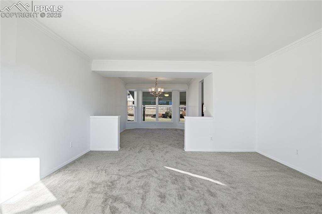 Spare room with a chandelier, light colored carpet, and ornamental molding