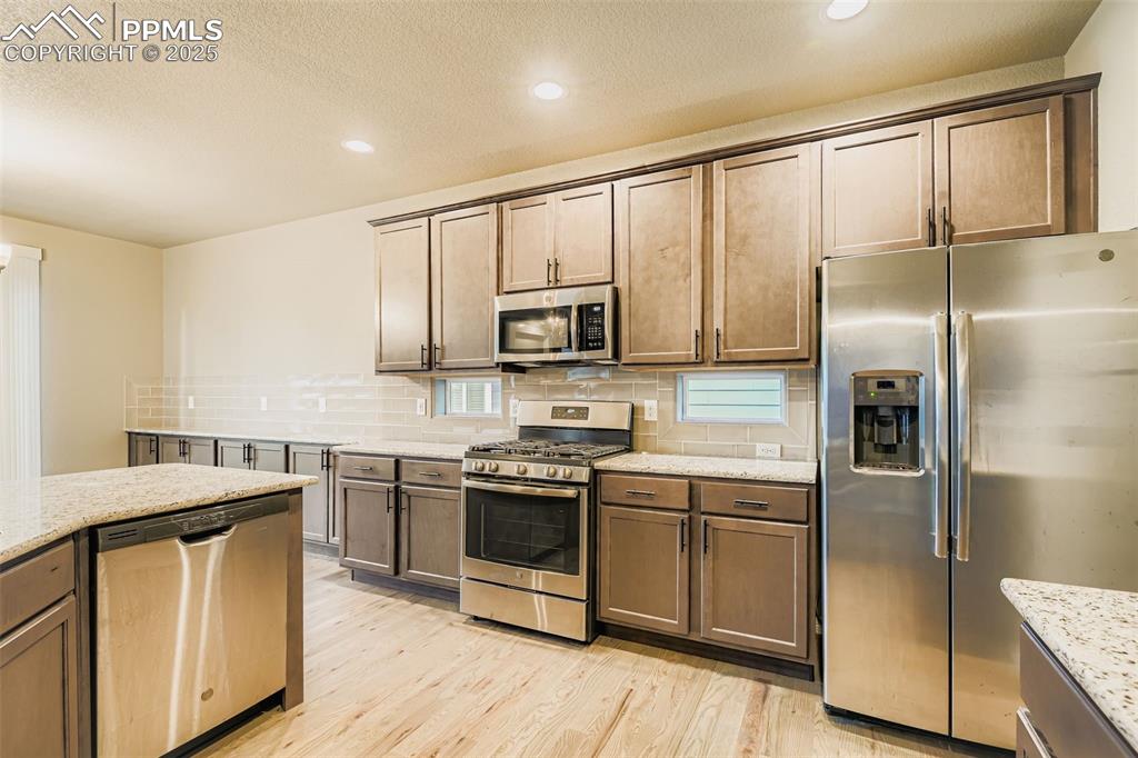Kitchen featuring stainless steel appliances, light wood-style floors, decorative backsplash, recessed lighting, and light stone counters