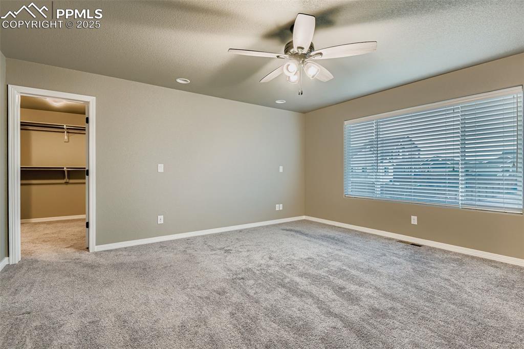 Unfurnished bedroom with a spacious closet, light colored carpet, a textured ceiling, and a ceiling fan