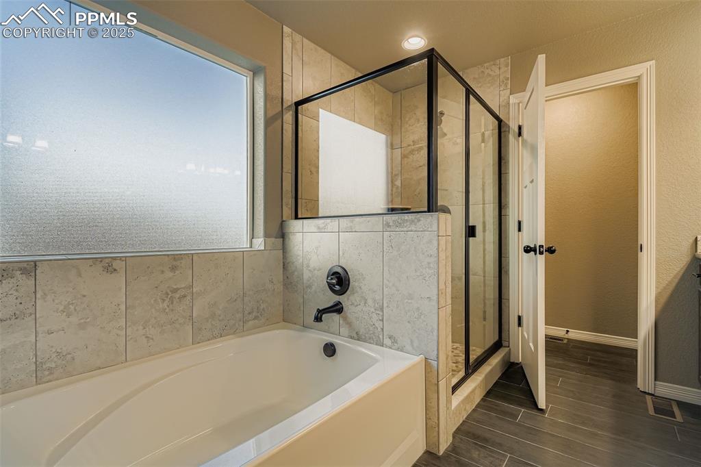 Full bathroom featuring a bath, a stall shower, and wood finish floors