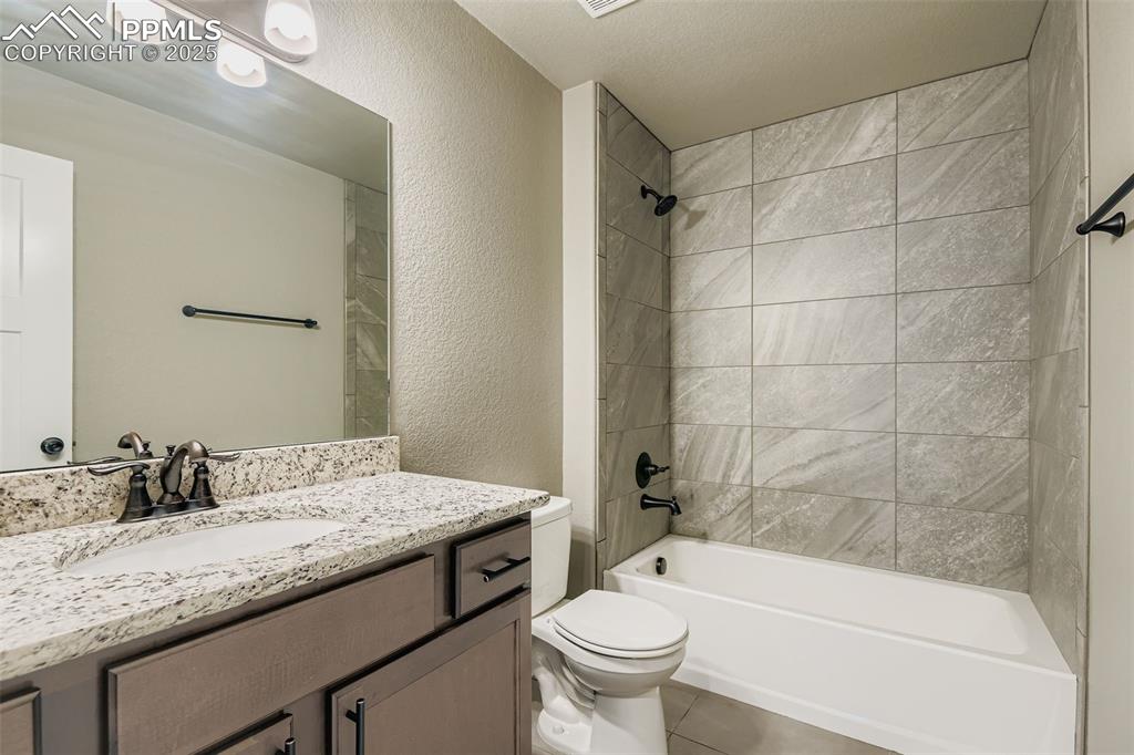 Full bath featuring a textured wall,  shower combination, vanity, and tile patterned floors