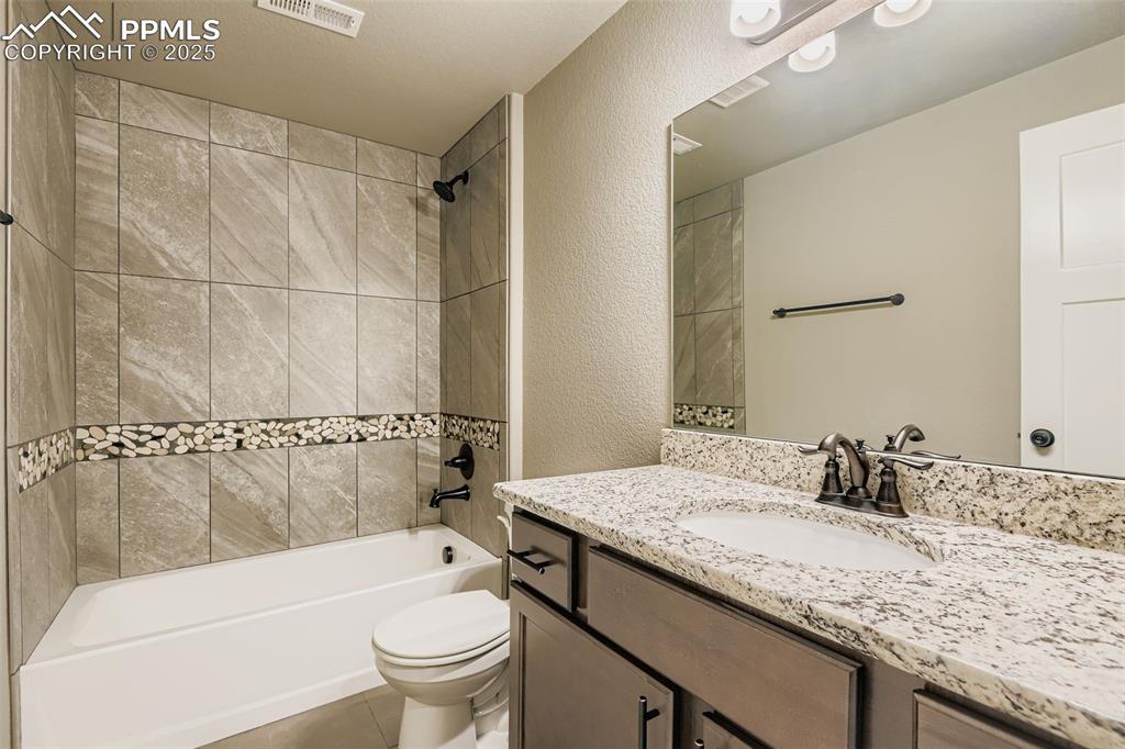 Bathroom featuring a textured wall, vanity, shower / tub combination, and light tile patterned flooring