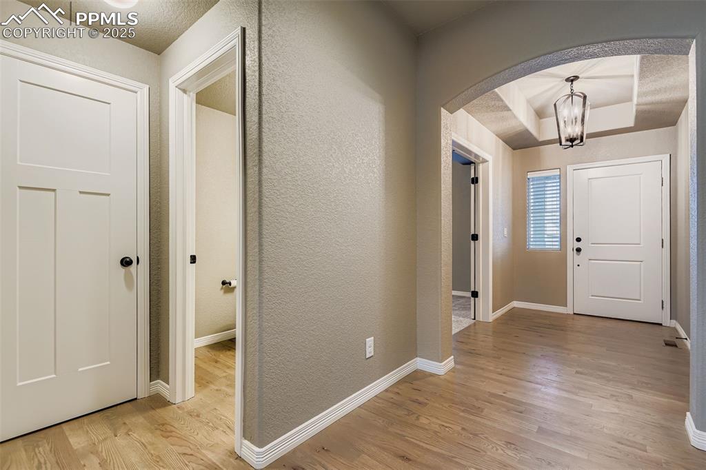 Foyer entrance with light wood-style floors, arched walkways, a chandelier, a textured wall, and a textured ceiling