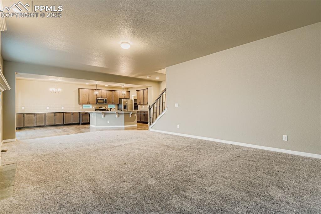 Unfurnished living room featuring light carpet, a chandelier, a textured ceiling, and stairs