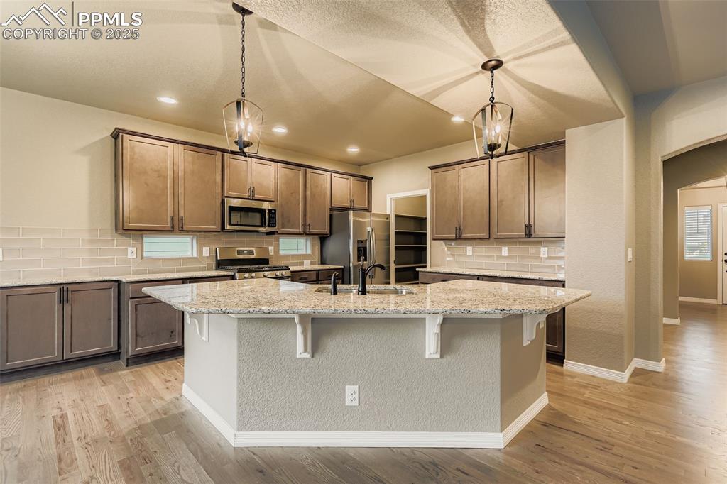 Kitchen featuring backsplash, arched walkways, appliances with stainless steel finishes, a kitchen bar, and light wood finished floors