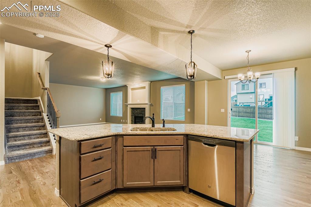 Kitchen with a textured ceiling, an island with sink, dishwasher, a fireplace, and decorative light fixtures