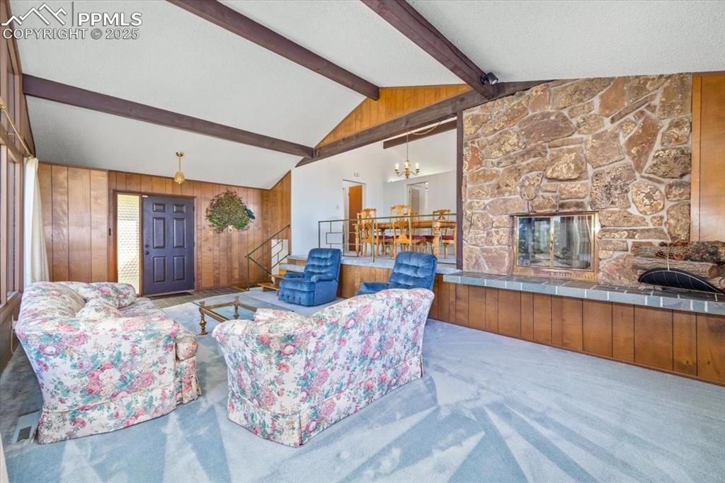 Carpeted living area with a fireplace, wooden walls, a textured ceiling, and a chandelier