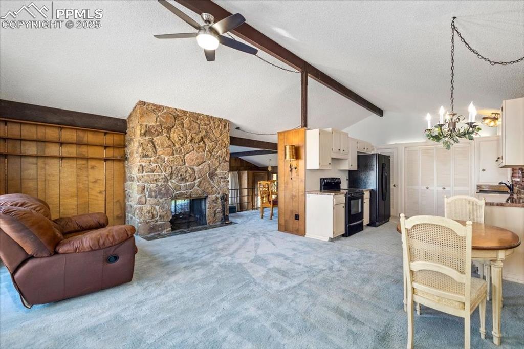Living room featuring light carpet, a textured ceiling, a stone fireplace, a chandelier, and ceiling fan