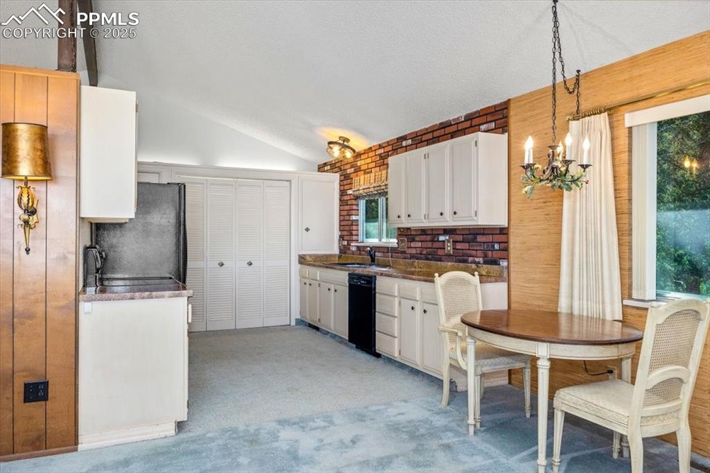 Kitchen with lofted ceiling, hanging light fixtures, light carpet, black appliances, and white cabinets